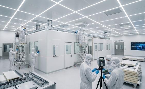 Gowned technicians installing cleanroom wall panels and surveying the layout with a laser instrument