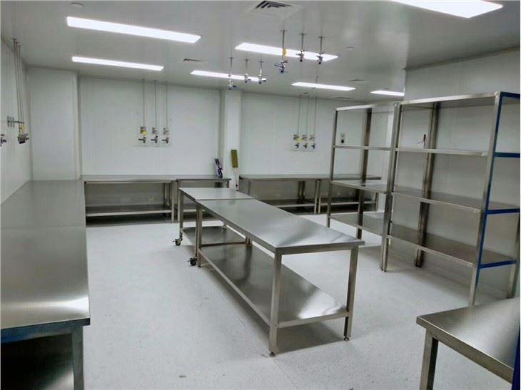Stainless-steel work tables and open racks arranged in a cleanroom